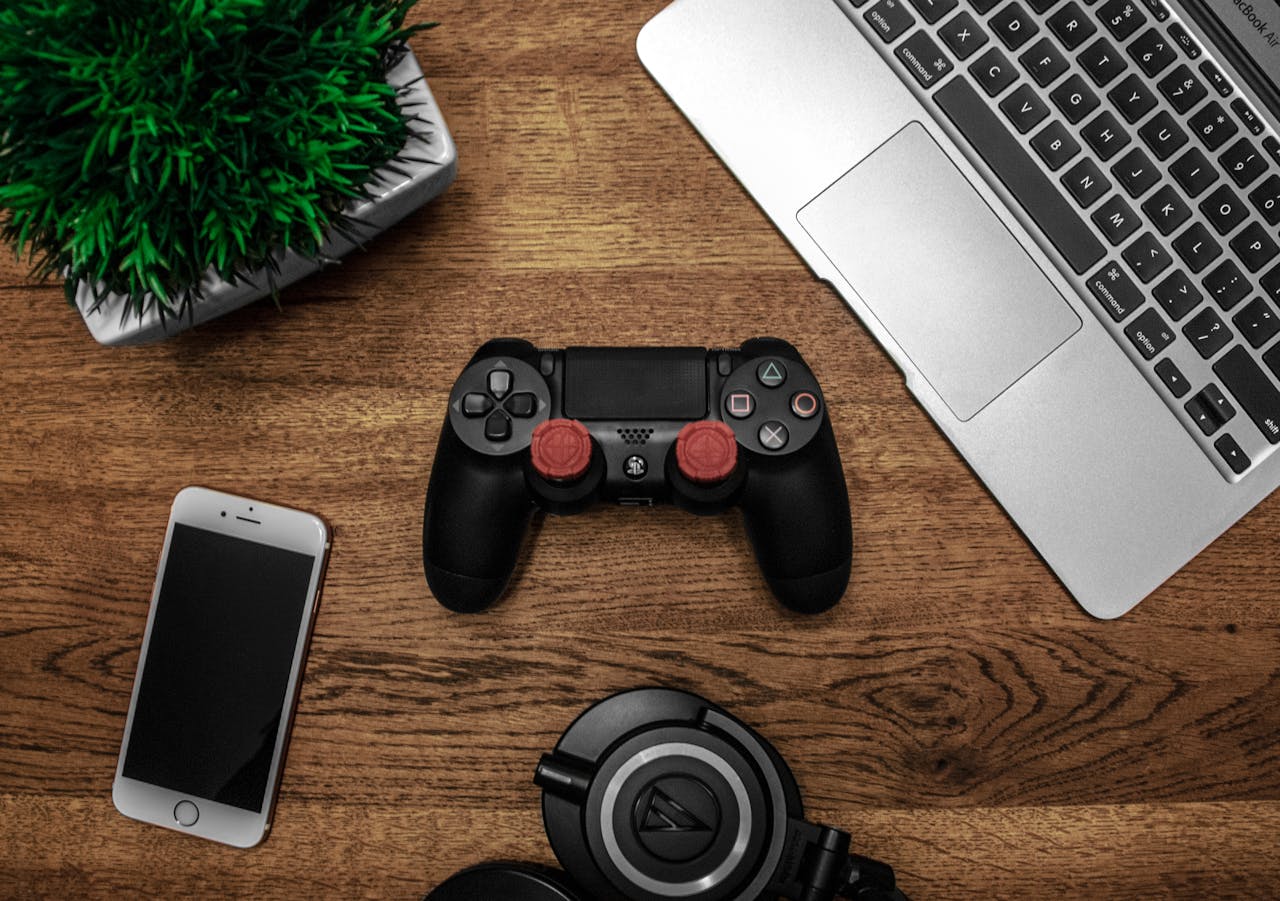 Home A flat lay photo showcasing a gaming console, laptop, smartphone, and headphones on a wooden tabletop.